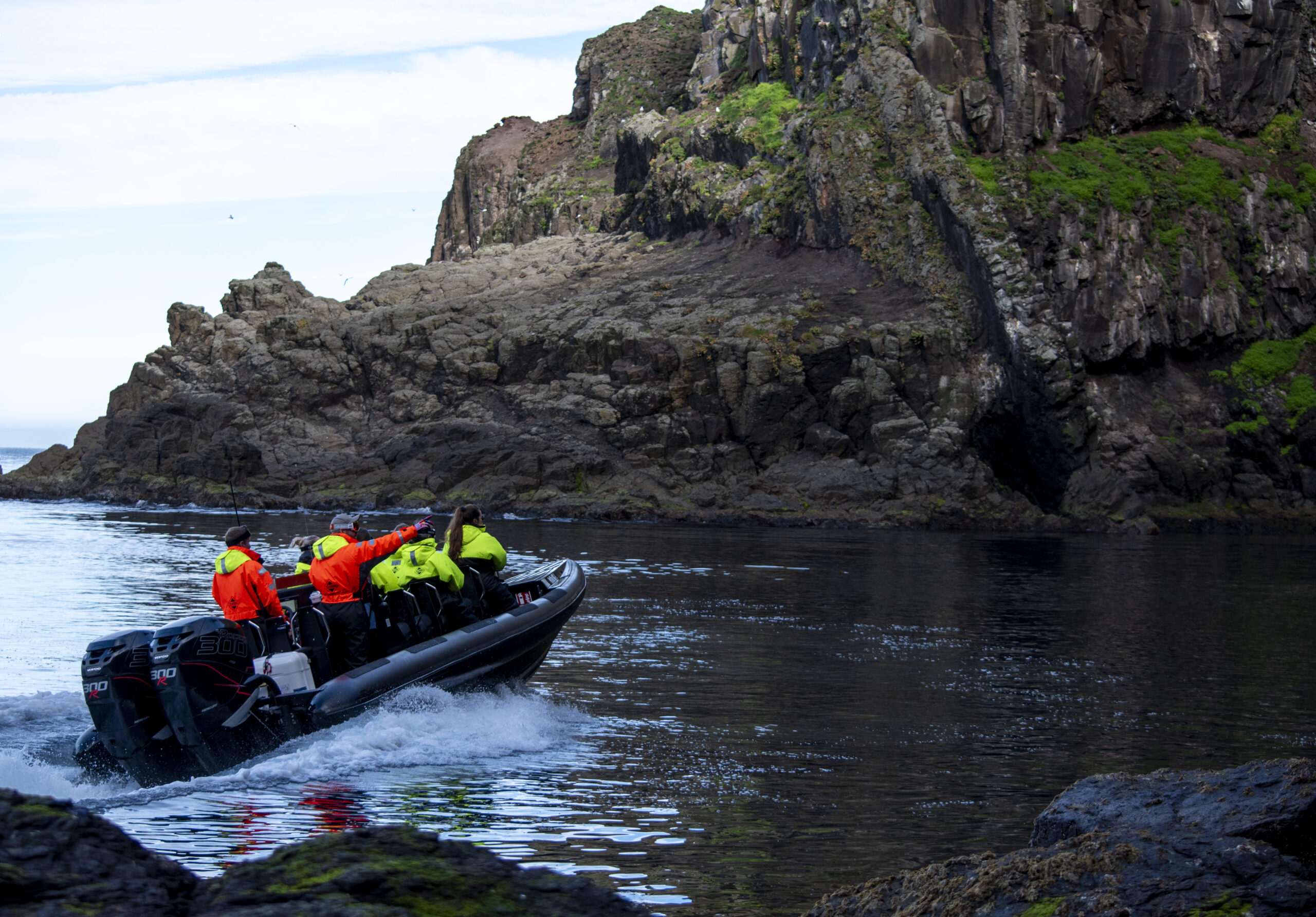 Boaters in bright jackets navigate near rocky cliffs on a calm sea, showcasing coastal adventure.