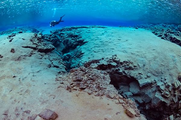 Diver exploring underwater tectonic plates at Silfra fissure, Iceland, in crystal clear blue water.