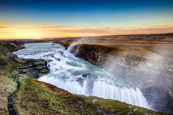 Majestic Gullfoss waterfall in Iceland with sunset sky, showcasing powerful cascading water and scenic landscape.