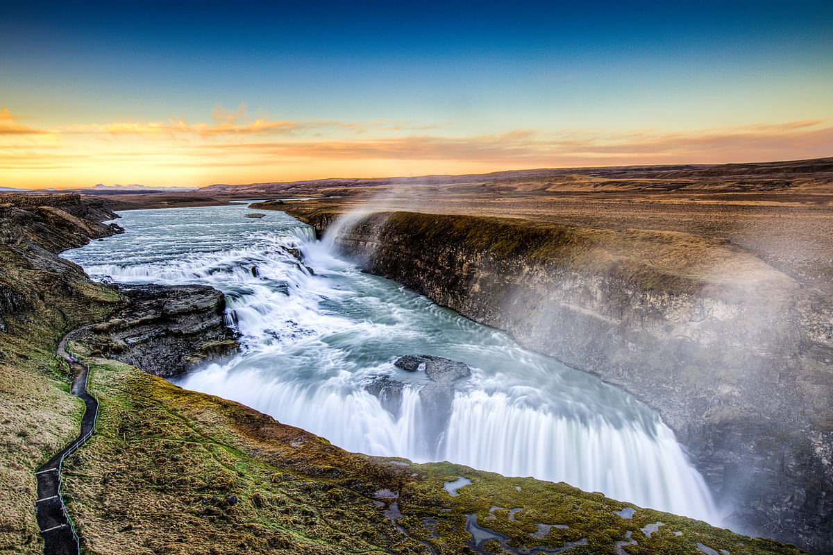 Majestic Gullfoss waterfall in Iceland with sunset sky, showcasing powerful cascading water and scenic landscape.