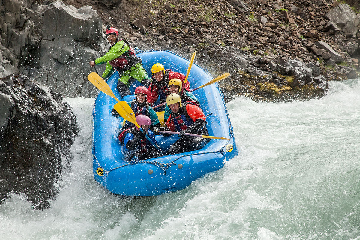 Group rafting in a blue inflatable boat navigating rocky rapids for adventure sports enthusiasts.