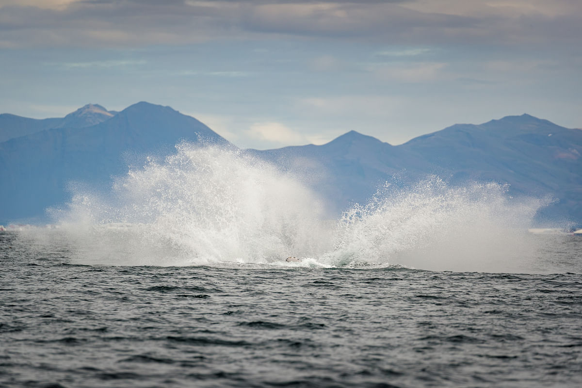 Water splash in the ocean with scenic mountain backdrop under cloudy sky.
