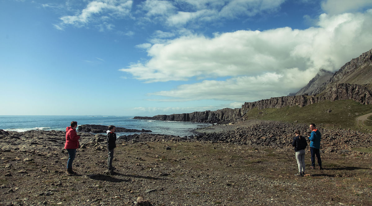 Four people enjoying a scenic rocky coastline with cliffs under a partly cloudy sky.
