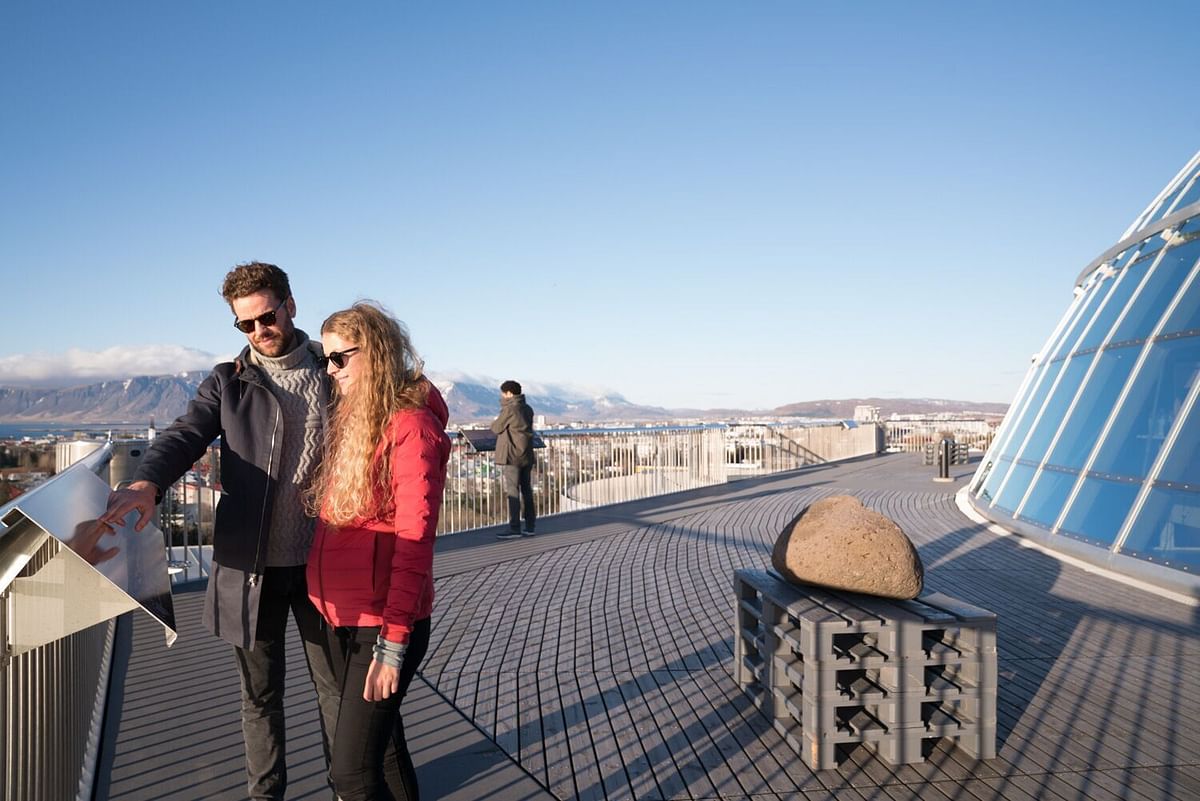 Couple enjoys panoramic city view from modern glass dome rooftop on sunny day.