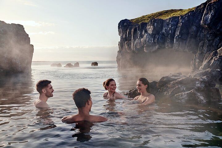 Four people enjoying a natural hot spring surrounded by rocky cliffs and mist, creating a serene and relaxing atmosphere.