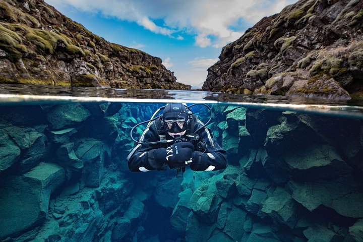 Diver in black gear explores clear waters between rocky cliffs beneath a blue sky.