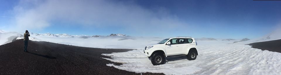 White SUV on snowy mountain road, person photographing scenic snowy landscape under clear blue sky. Adventure travel.