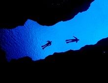 Silhouettes of divers floating in vibrant blue water inside a dark cave, creating a striking contrast.