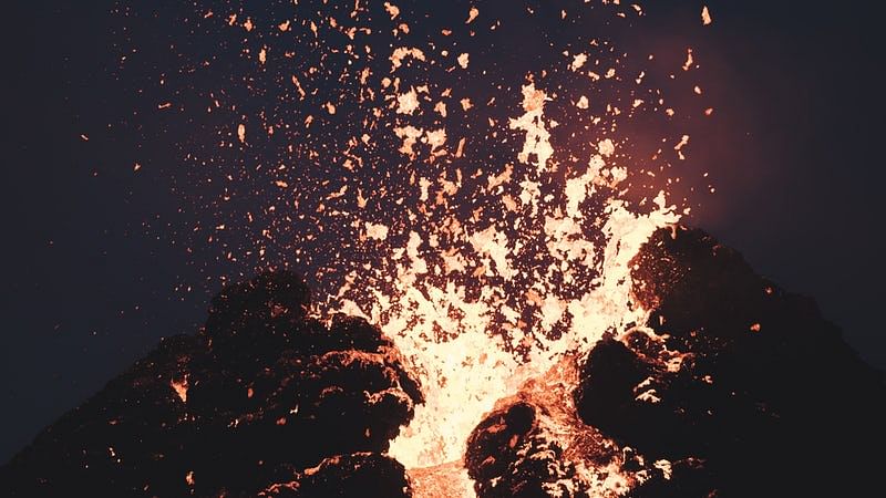 Volcano erupting with bright lava and ash against a dark sky, illustrating powerful volcanic activity.