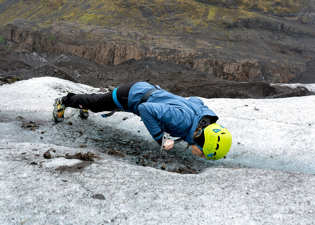 Person drinking water from a glacier using an ice axe in an adventurous glacier climbing trip, wearing a helmet.