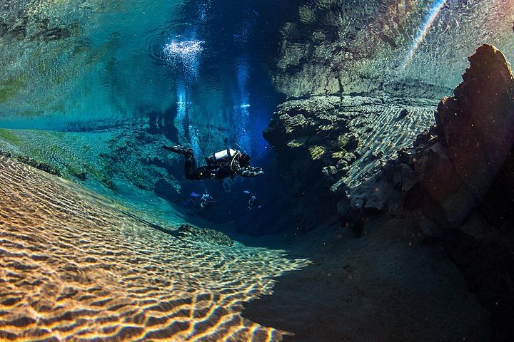 Scuba diver explores vibrant underwater cavern with clear blue water and rocky formations.