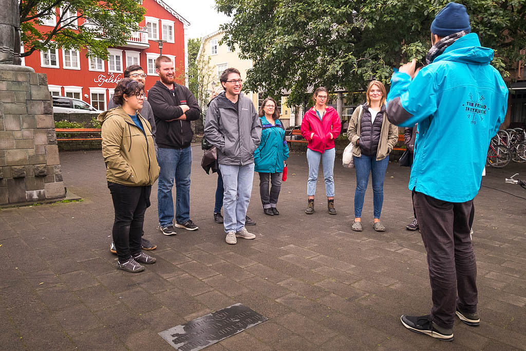 Group of tourists on a guided walking tour in a city square, led by a tour guide in a blue jacket.
