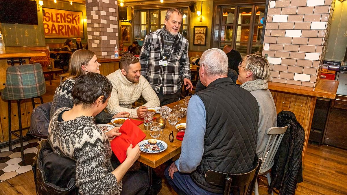 Group of people enjoying a meal at a cozy restaurant, engaged in conversation with a server.