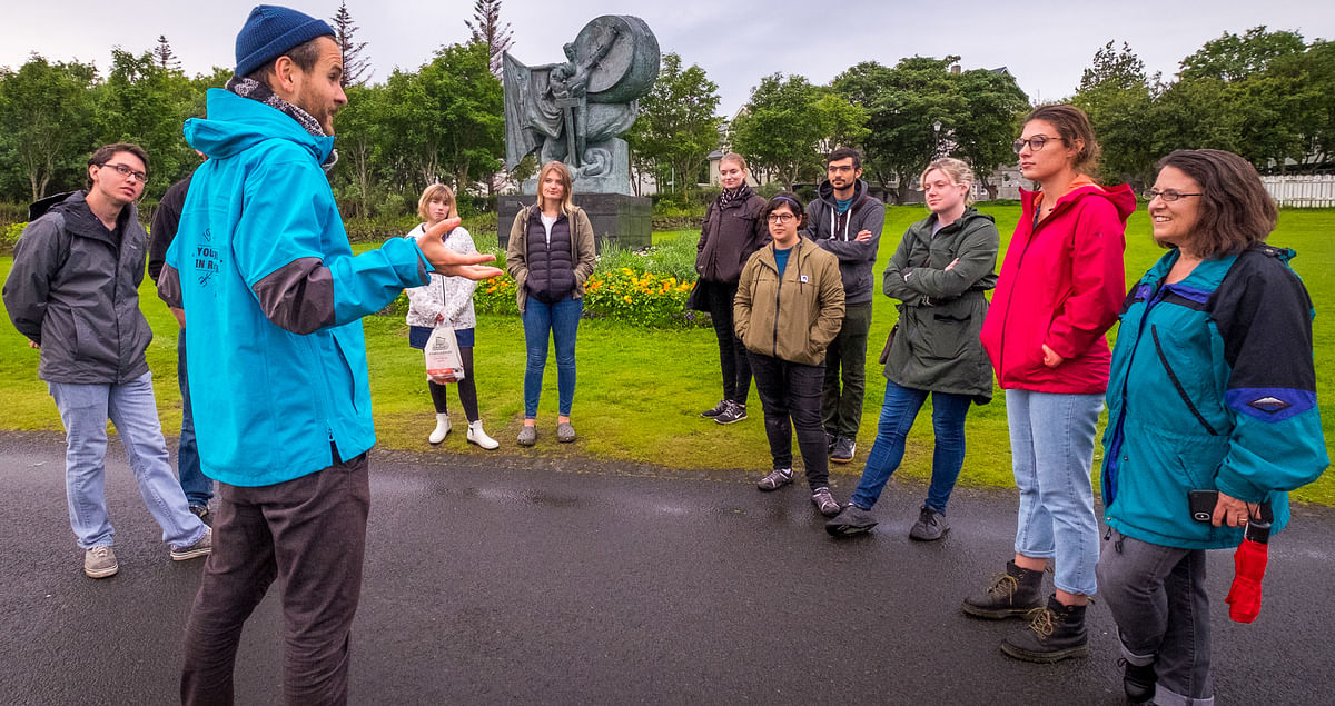 Outdoor tour guide speaking to a group in a park with a sculpture in the background.