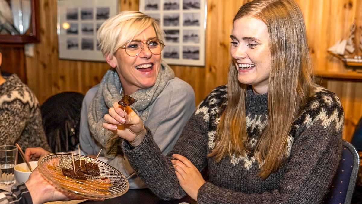 Two people enjoying traditional food in a cozy restaurant, wearing warm sweaters and smiling.