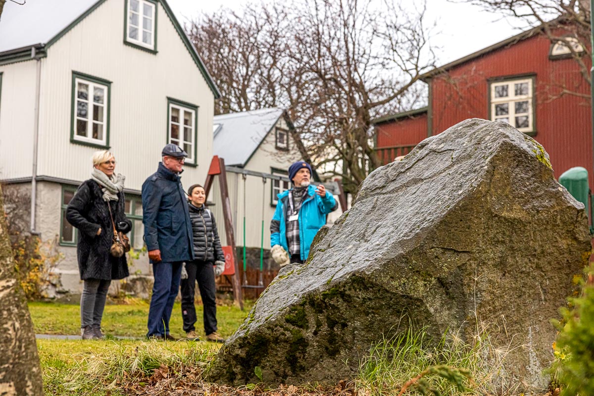 Group on an outdoor tour beside rock, with historic buildings in the background.