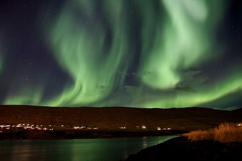 Northern Lights illuminate the night sky over a serene landscape and reflective water.