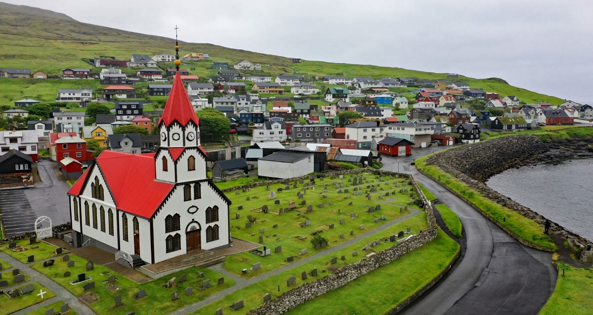 Red-roofed church and colorful village in Tórshavn, Faroe Islands, with cemetery and scenic coastal view.