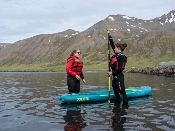 Two people prepare for paddleboarding in a scenic mountain lake setting.