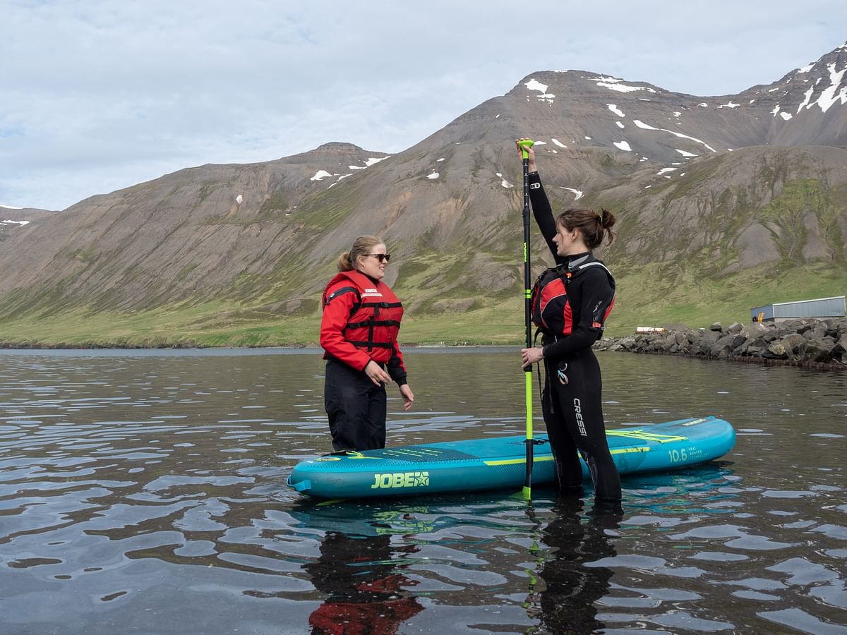 Two people prepare for paddleboarding in a scenic mountain lake setting.