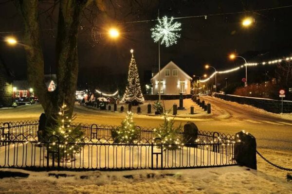 Cozy winter village with festive lights and snow, featuring a decorated Christmas tree and illuminated streets at night.