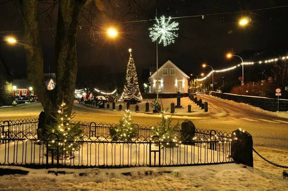 Cozy winter village with festive lights and snow, featuring a decorated Christmas tree and illuminated streets at night.