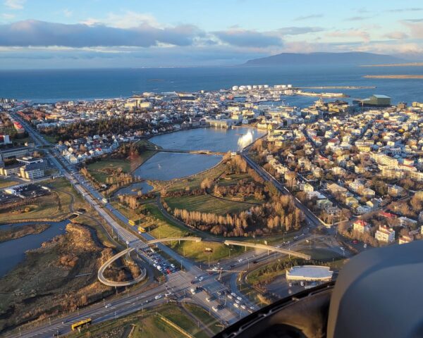 Aerial view of Reykjavik, Iceland, showcasing cityscape, coastlines, and roads under a bright morning sky.