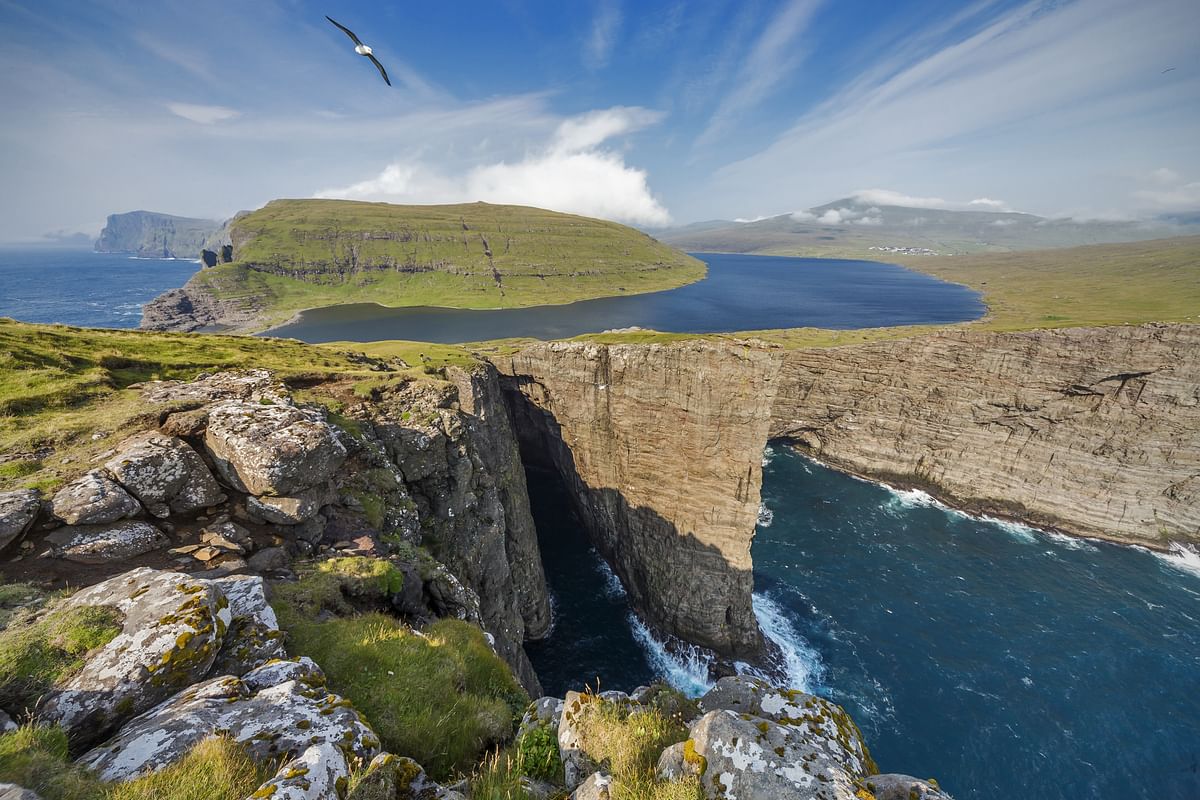Dramatic cliffside view of Sørvágsvatn Lake meeting the sea in the Faroe Islands under a clear blue sky.