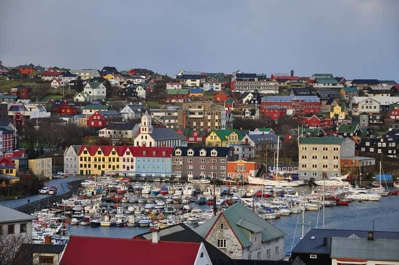 Colorful harbor town with boats and vibrant houses under a cloudy sky, offering a picturesque coastal view.