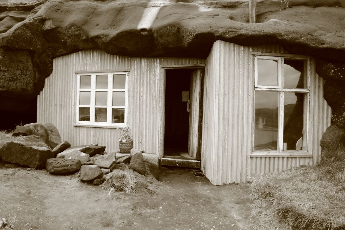 Rustic sepia-toned cottage with stone wall, two windows, and a plant in front. Vintage charm and natural setting.