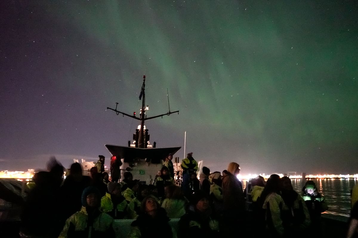 People on a ship watching the Northern Lights illuminate the night sky over the ocean.