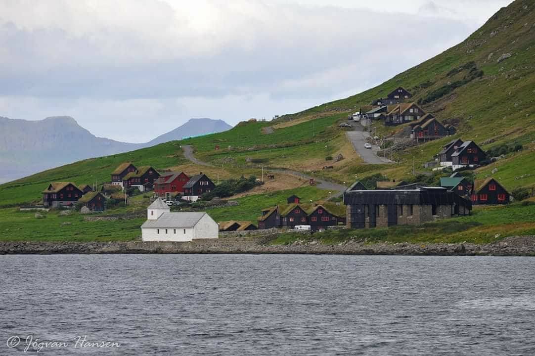 Scenic view of a remote village with traditional houses on a green hillside near the water, lush landscape in the background.