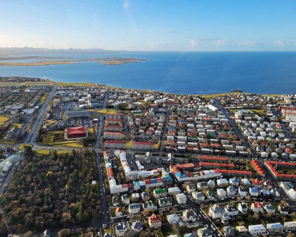 Aerial view of a colorful coastal city by the sea with sprawling residential and commercial areas under a clear sky.