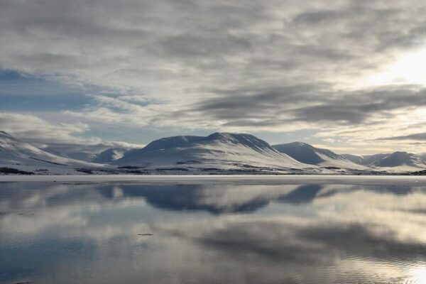 Snowy mountains and cloudy sky reflected in a calm lake, creating a serene winter landscape.