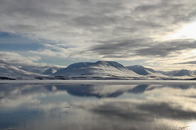 Snowy mountains and cloudy sky reflected in a calm lake, creating a serene winter landscape.