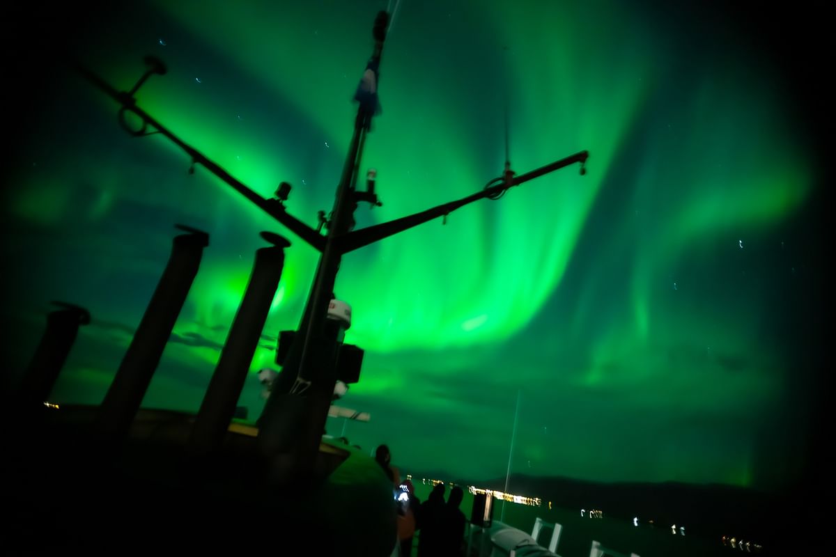 Silhouette of a ship under vibrant green Northern Lights in the night sky.