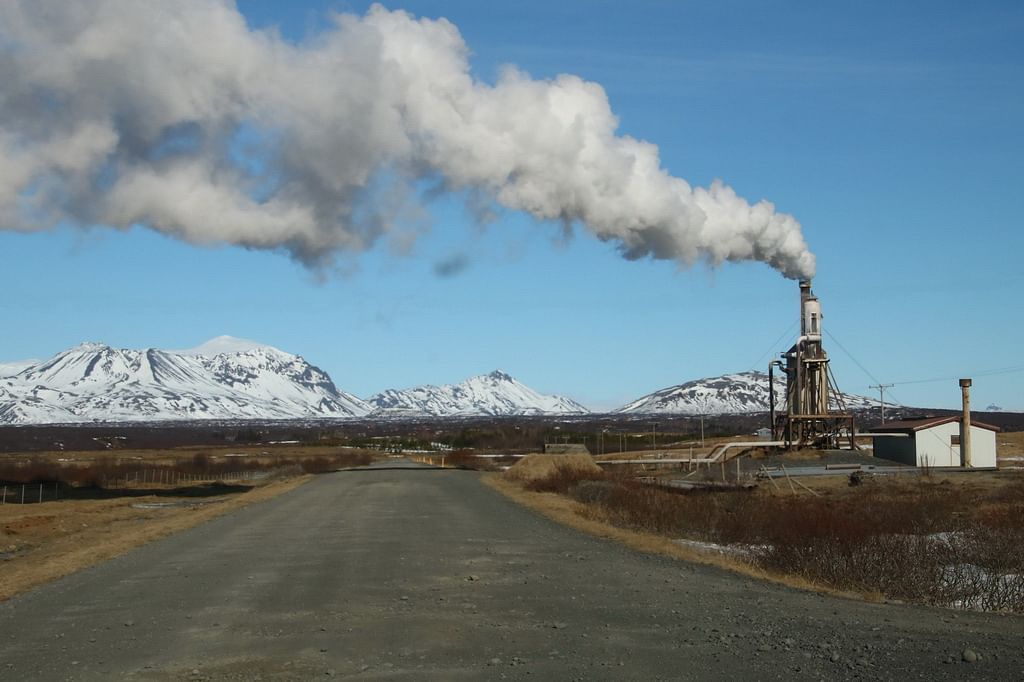 Geothermal power plant with steam against snowy mountain backdrop on a clear day.