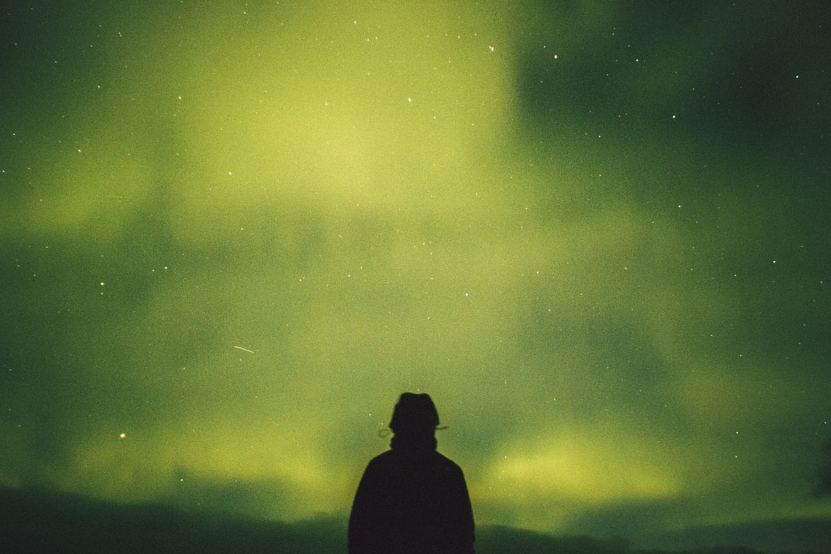 Silhouette of a person watching the Northern Lights under a starry night sky.