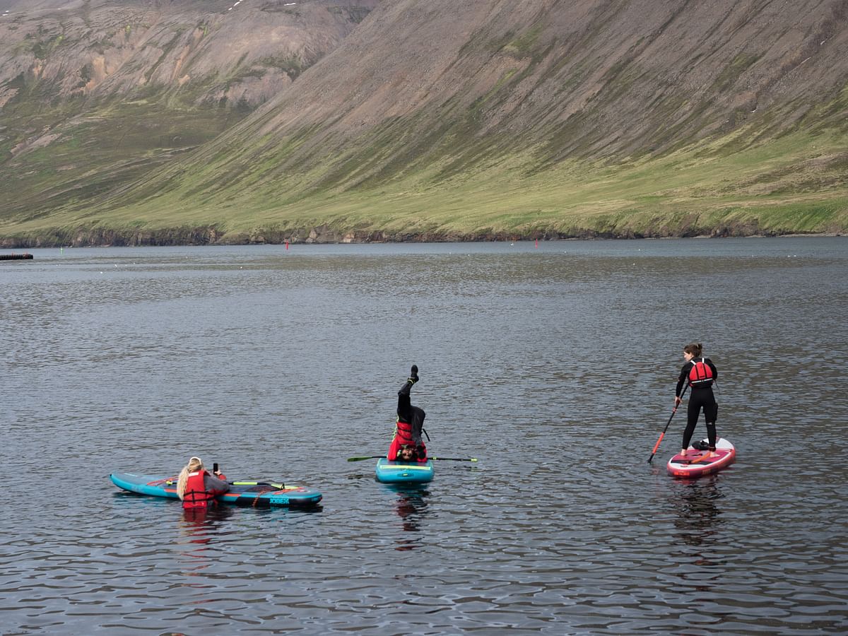 Three people paddleboarding in a scenic lake surrounded by mountains.