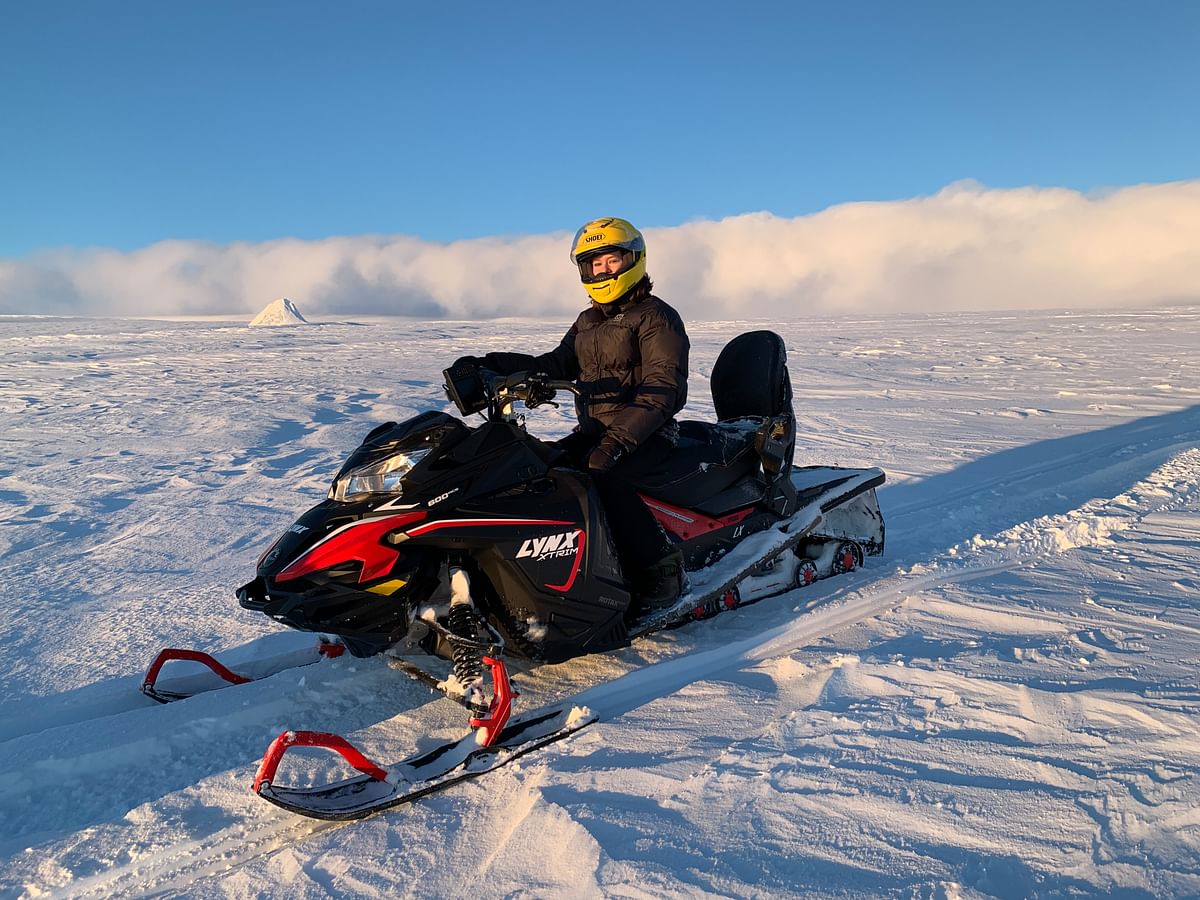 Person riding a Lynx snowmobile on a snowy landscape under a clear blue sky.