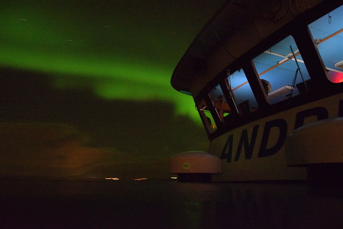 Boat under Northern Lights illuminating the sky with vibrant green hues at night.