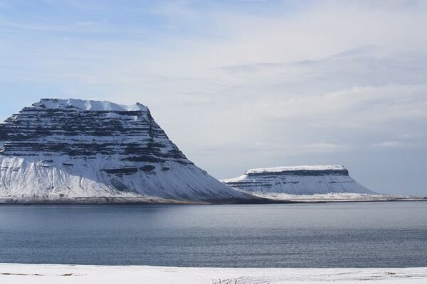 Snow-covered mountains near a calm sea under a partly cloudy sky, creating a serene winter landscape.