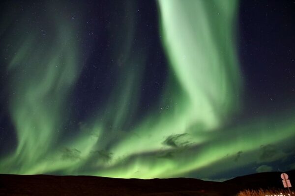 Green Northern Lights dancing in a starry night sky over a dark landscape.