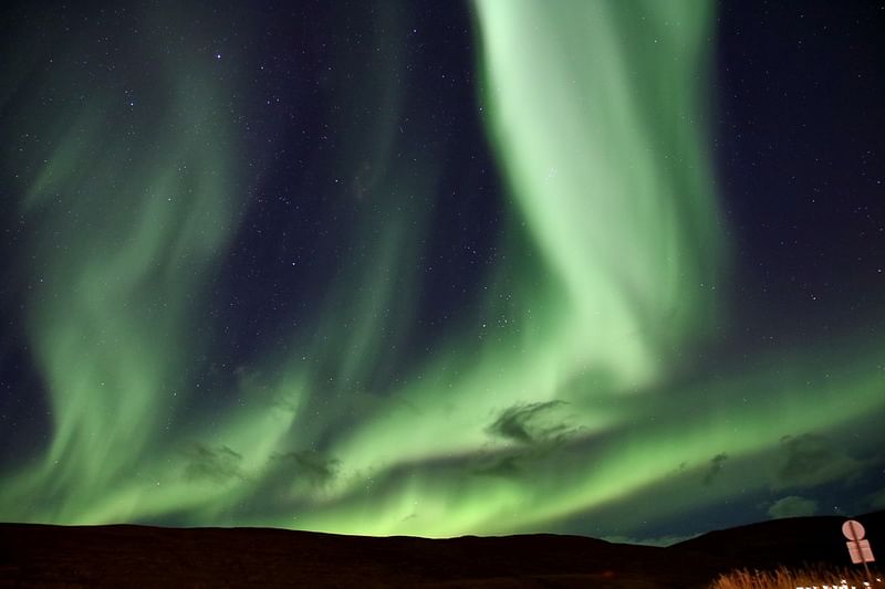 Green Northern Lights dancing in a starry night sky over a dark landscape.