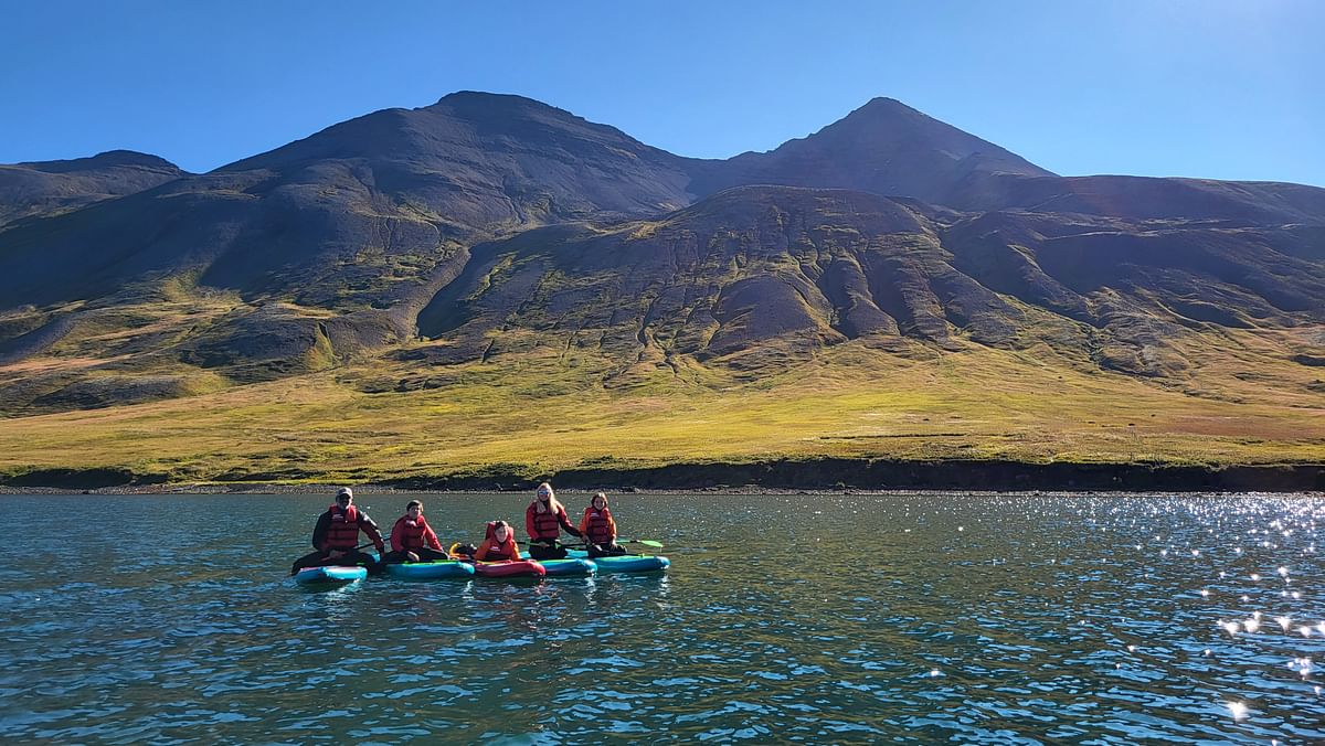 Kayakers in life jackets paddle on a serene lake with majestic mountains in the background.