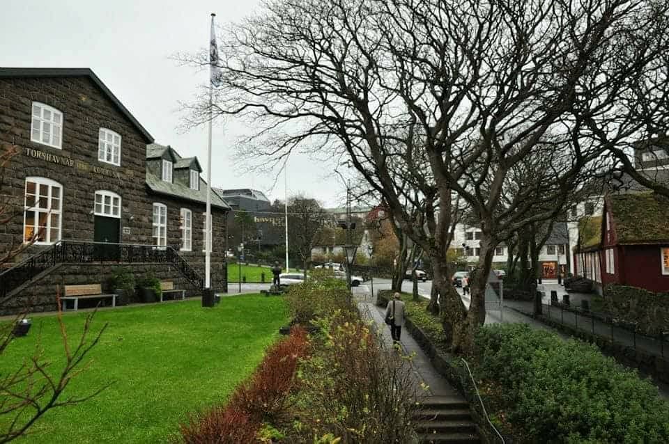 Historic building and winter trees in Tórshavn, Faroe Islands, with a person walking along the path.