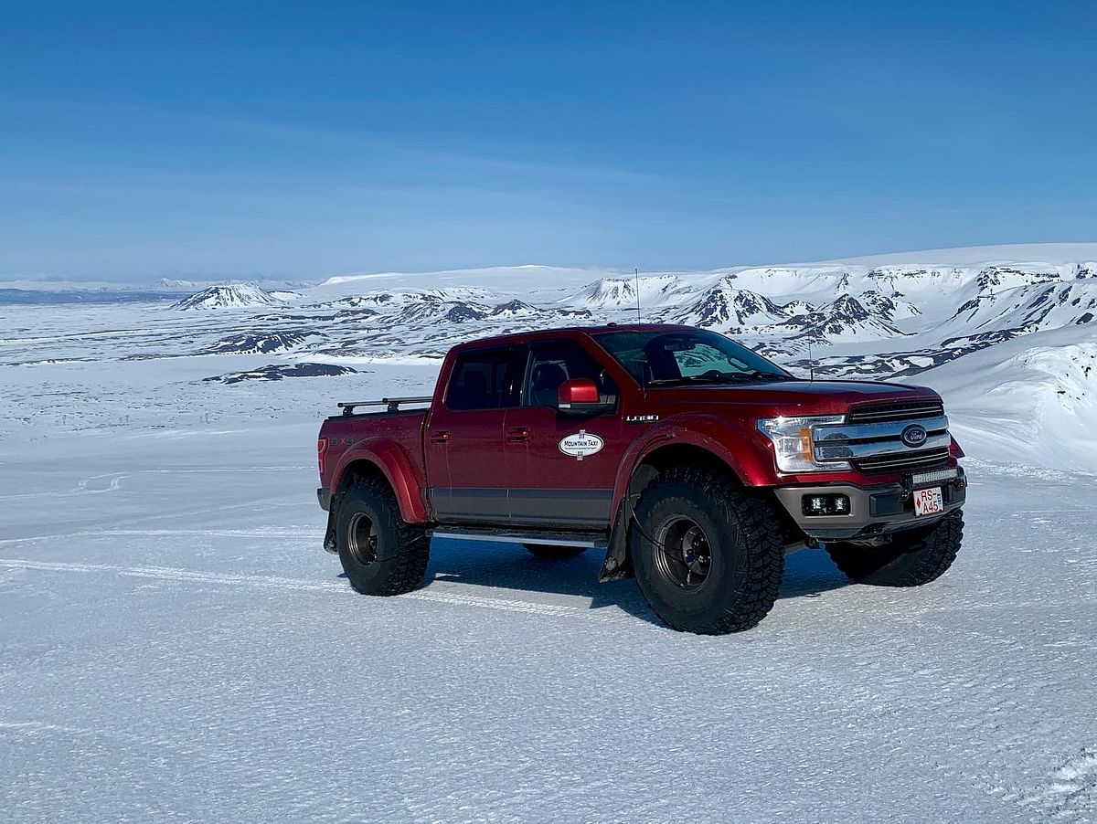 Red pickup truck on a snowy landscape with mountains in the background under a clear blue sky.