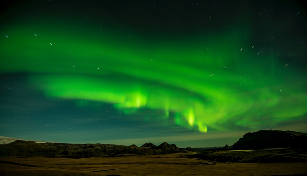 Vibrant green Northern Lights in a clear night sky over a rugged landscape.
