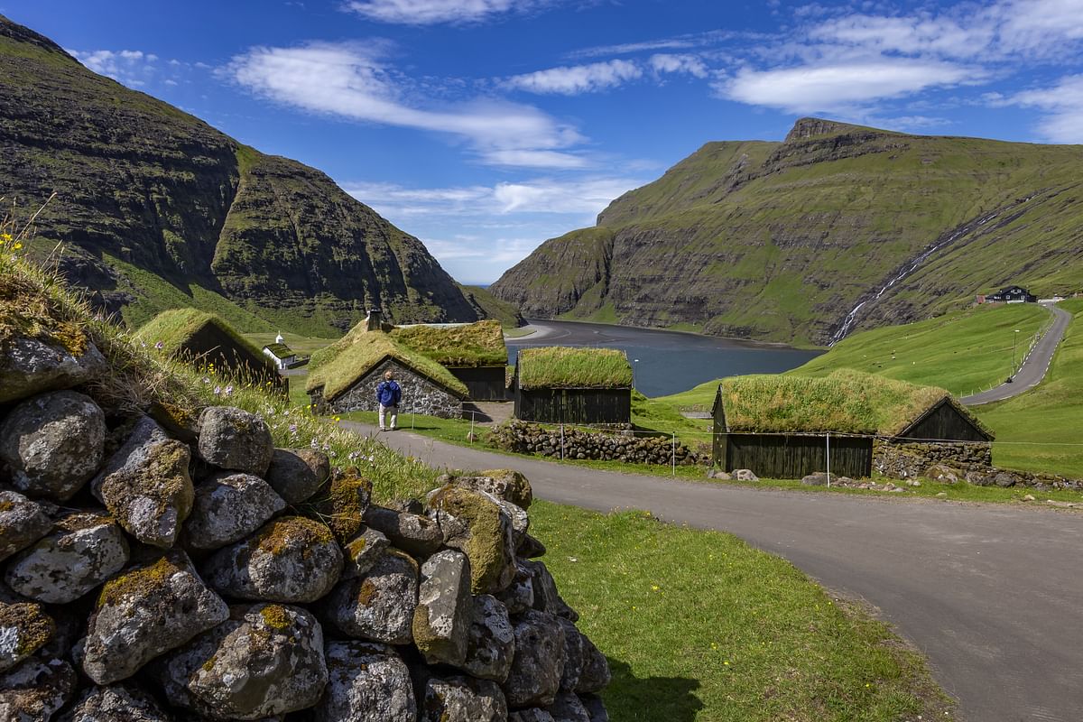 Scenic view of grass-roofed huts and mountains in Saksun, Faroe Islands, under a blue sky.