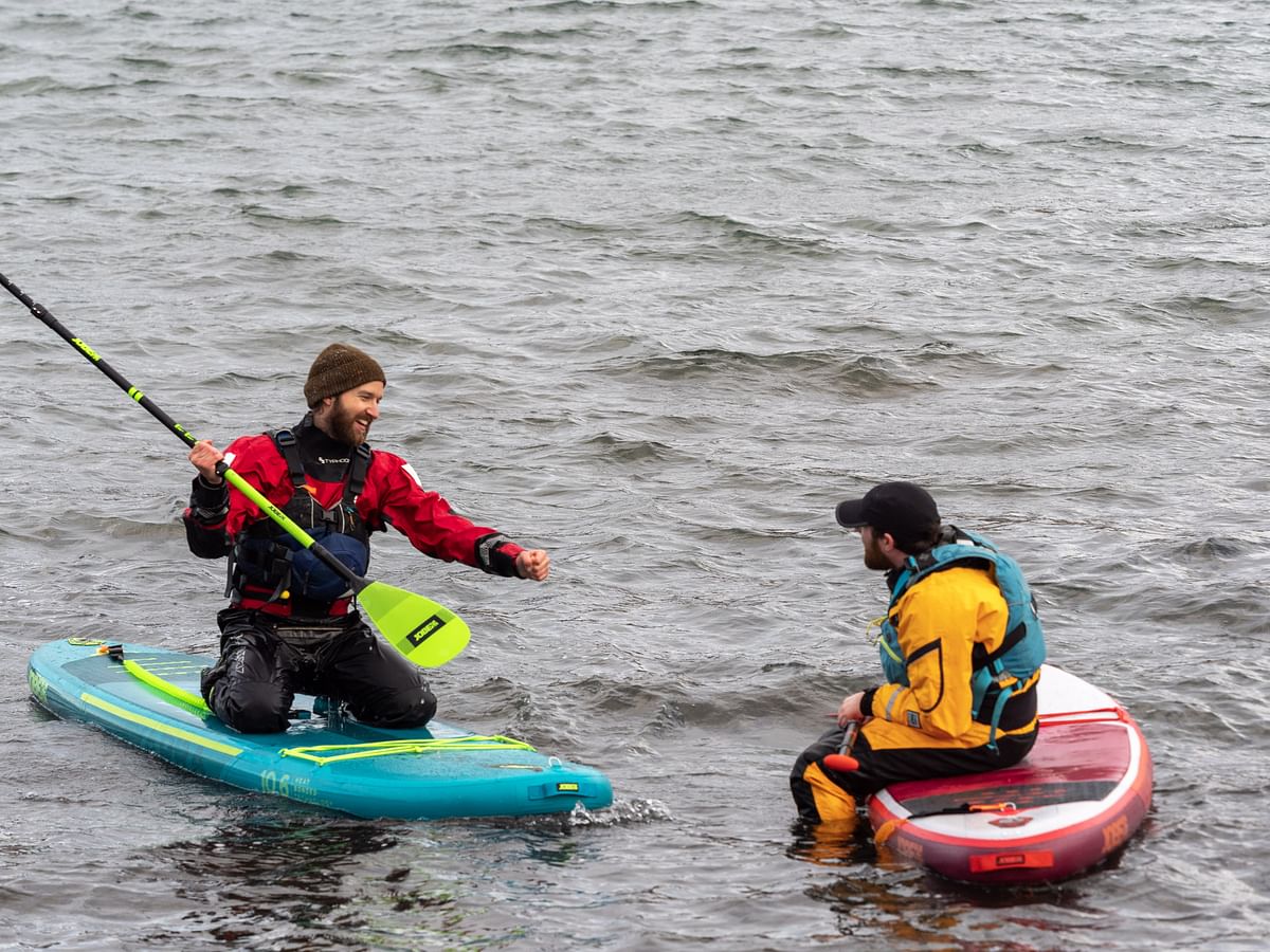 Two people paddleboarding in wetsuits, sharing a moment on the water.